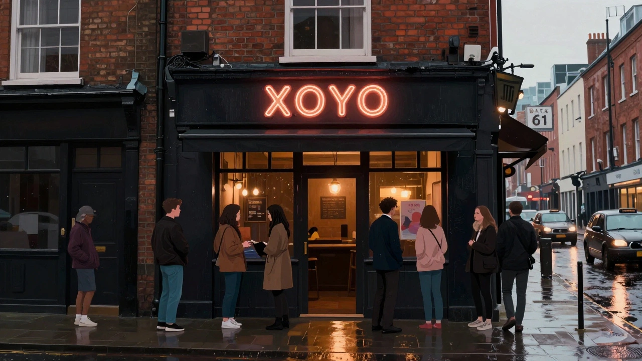 XOYO nightclub exterior at night with people waiting to enter, modest neon sign, rainy Shoreditch street, no corporate branding.